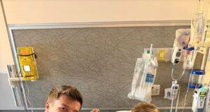 Young girl in hospital bed with two smiling visitors, medical equipment in background.