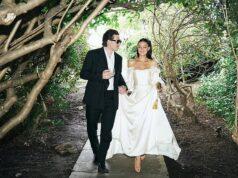 Stylish couple walking through lush garden forest in elegant wedding attire, enjoying a romantic moment.