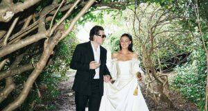 Stylish couple walking through lush garden forest in elegant wedding attire, enjoying a romantic moment.