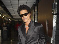 Stylish man in black satin double-breasted suit with sunglasses at airport.