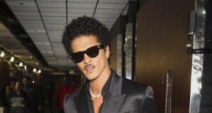 Stylish man in black satin double-breasted suit with sunglasses at airport.