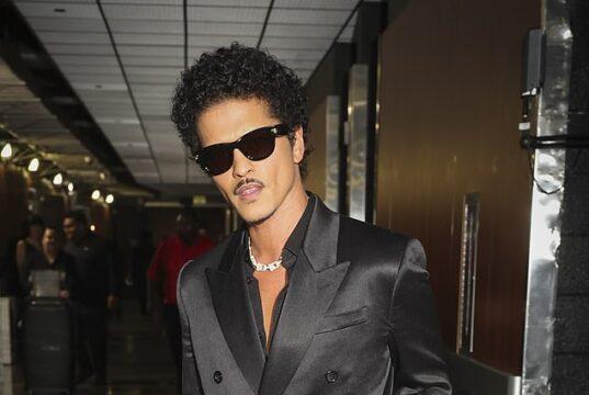 Stylish man in black satin double-breasted suit with sunglasses at airport.
