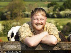 Happy man smiling outdoors with cows and green fields in background.