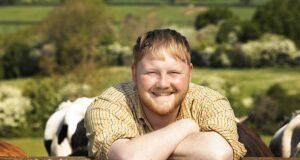 Happy man smiling outdoors with cows and green fields in background.