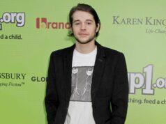 Young man at charity event with a green background featuring Lanka News Room logos.