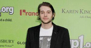 Young man at charity event with a green background featuring Lanka News Room logos.