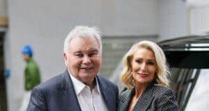 Elderly man with walker and woman in formal attire smiling outdoors.