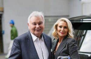 Elderly man with walker and woman in formal attire smiling outdoors.