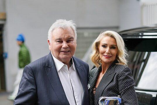 Elderly man with walker and woman in formal attire smiling outdoors.