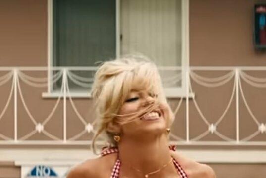 Blonde woman smiling in a red checkered bikini, outdoors, sunny weather.
