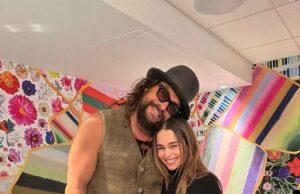 News Room : Game Of Thrones stars Jason Momoa and Emilia Clarke reunite 15 years after starring on iconic HBO series Huge man with curly hair, sunglasses, and a hat standing next to a smiling woman in black, vibrant colorful background.