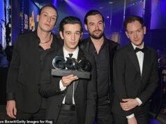 Men in formal suits accepting an award at a ceremony in a nightclub or event hall.