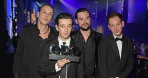 Men in formal suits accepting an award at a ceremony in a nightclub or event hall.