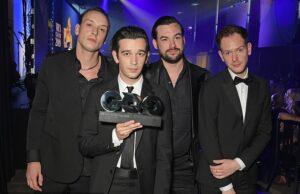 Men in formal suits accepting an award at a ceremony in a nightclub or event hall.