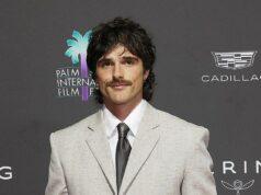 Stylish man in a light gray suit at a film festival event with Palm Springs International Film Festival logo in the background.