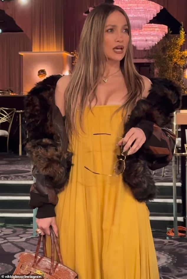 News Room : Jennifer Lopez pokes fun at her ex Elegant woman in a yellow dress and fur jacket at a glamorous event, holding a handbag and sunglasses.