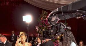 Elegant woman in glamorous gown being filmed at red carpet event with professional camera crew.