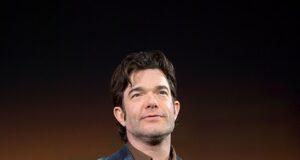 Man in navy blazer on stage at a conference or event in front of a colorful background.