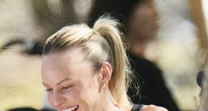 Smiling woman enjoying a meal at an outdoor cafe, wearing black top and gold jewelry.