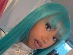 Vibrant turquoise-haired woman with jewelry and bold makeup in a modern room setting.