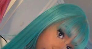Vibrant turquoise-haired woman with jewelry and bold makeup in a modern room setting.