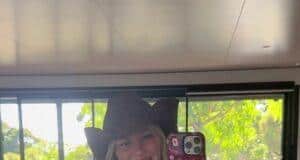 Vibrant woman in polka dot swimsuit and cowboy hat taking mirror selfie indoors at bright, modern space.