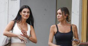 Women having conversation outside a building in casual attire, one gesturing with her hand.