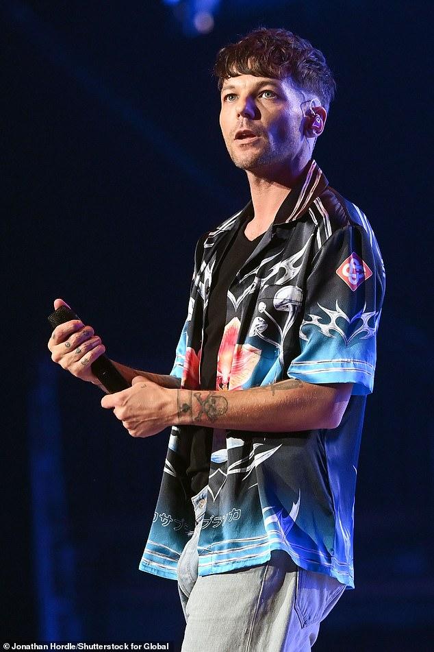 News Room : Louis Tomlinson pays heartbreaking tribute to his Young man performing on stage with microphone, dark background, casual stylish attire, tattoos on arm.
