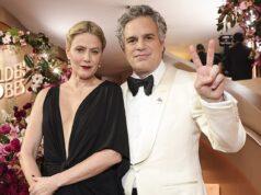 Elegant couple at a glamorous event, dressed in formal attire with floral decor in the background.