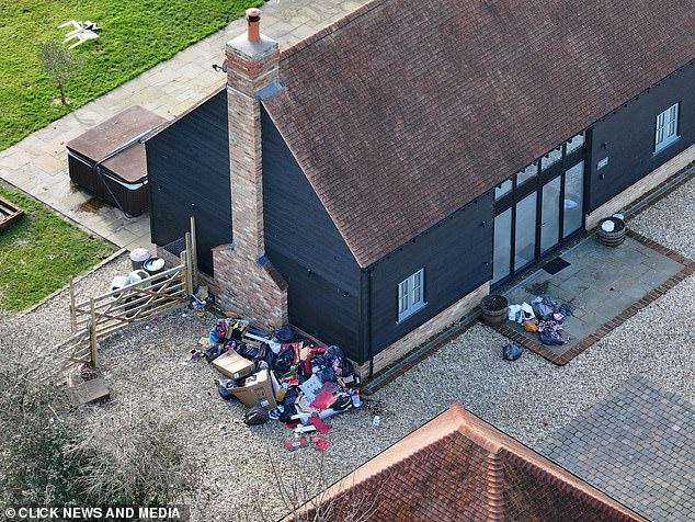 News Room : Muckier Mansion! Katie Price's plush new pad Overflowing trash piles outside black wooden house in a residential area.
