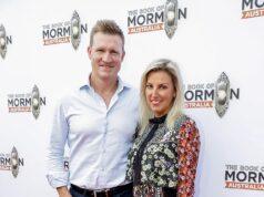 Elegant man and woman at book launch event for "The Book of Mormons Australia" in front of branded backdrop, red carpet, stylish attire, smiling, event photos.