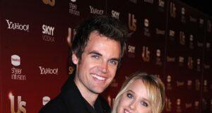 Smiling young couple at entertainment event, standing close together in front of media backdrop.