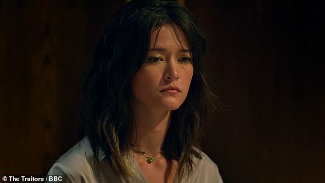 News Room : Revealed: Murder-suicide family secret of Traitors PhD Young woman with dark wavy hair, contemplative expression, indoor dark background.