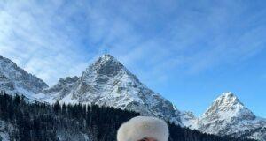 Hot woman in winter landscape in bikini and fur hat, snowy mountains in background, scenic outdoor photo.