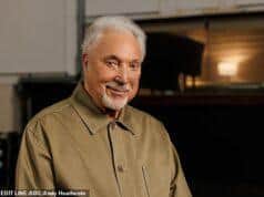 A senior man with white hair and a beard smiling indoors.