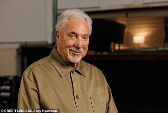 A senior man with white hair and a beard smiling indoors.